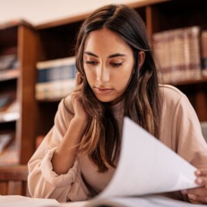 woman reading papers with books in background