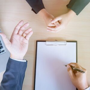 hands clasped with set of hands writing with a clip board and pen